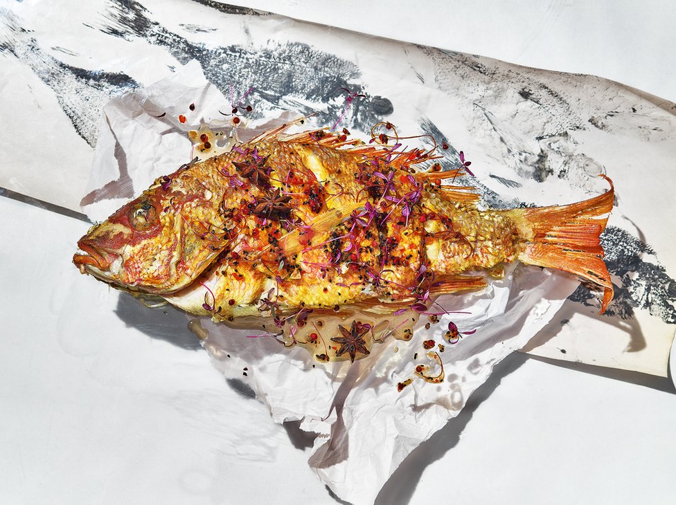 A cooked fish on paper with abstract fish prints on