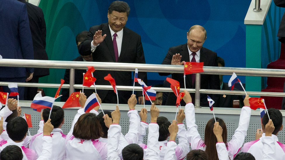Президент России Владимир Путин (справа) и президент Китая Си Цзиньпин машут зрителям во время товарищеского матча между молодежными хоккейными командами Китая и России 8 июня 2018 г. в Тяньцзине, Китай