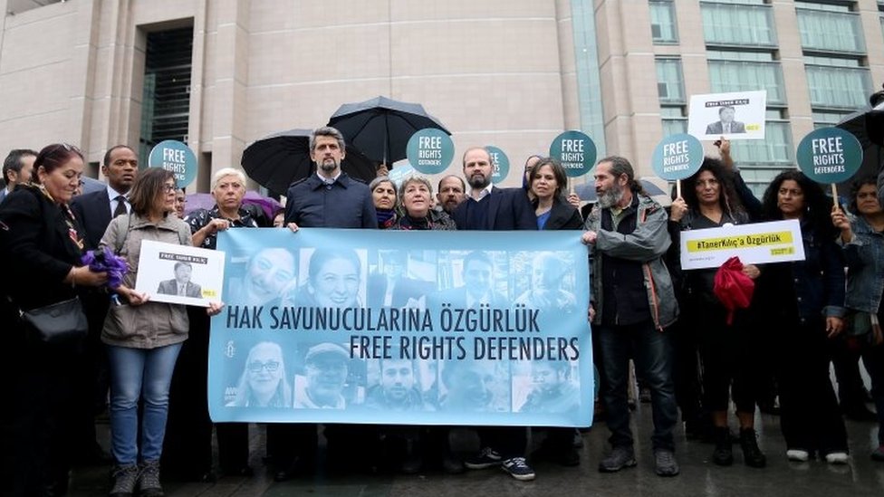 Люди у стамбульского суда держат плакаты и транспарант с фотографиями обвиняемых активистов. Фото: 25 октября 2017 г.