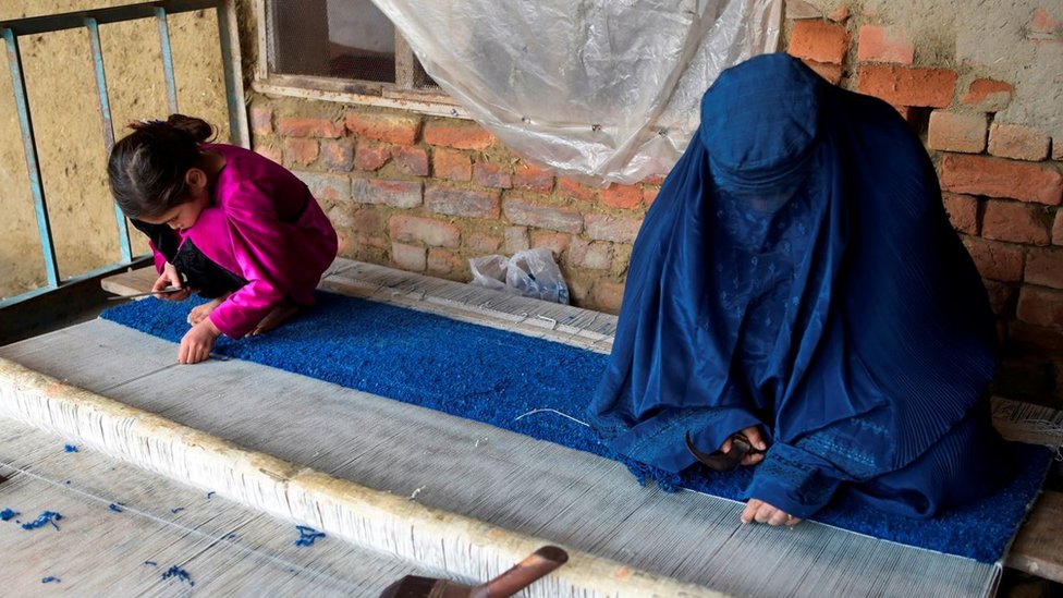 لاجئة وطفلتها تعملان في حياكة قطعة من السجاد