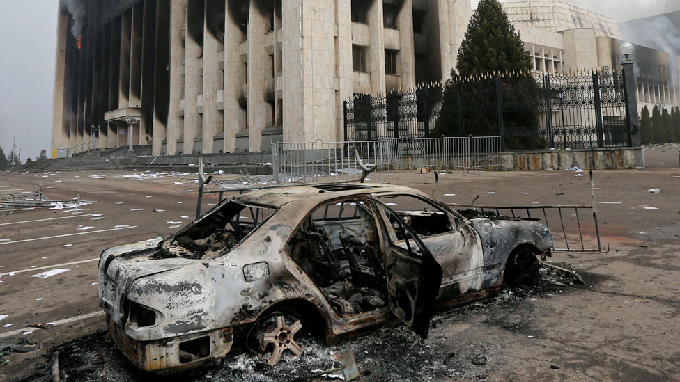 A man takes a picture as a burned car is seen in front of the mayor's office building which was torched during protests triggered by fuel price increase in Almaty, Kazakhstan January 6, 2022