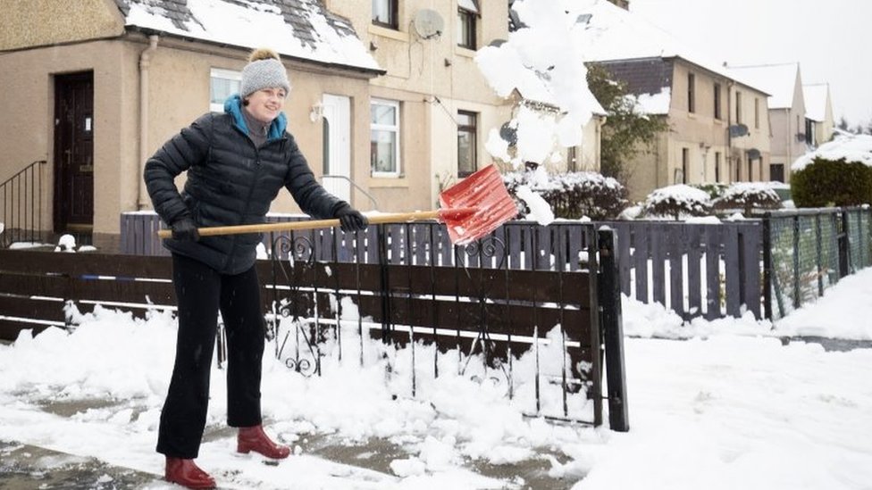 امرأة تزيل الثلوج المتراكمة في حديقة منزلها