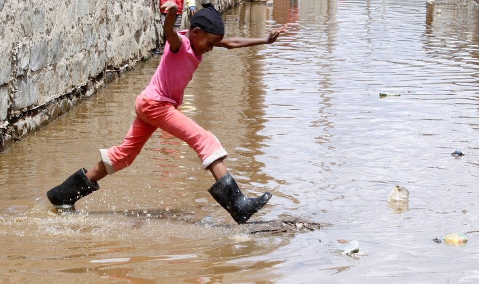 A child jumps through floodwaters near houses.