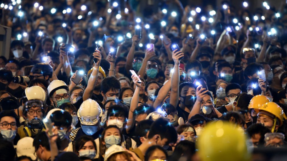 Протестующие держат свои мобильные телефоны, когда они собираются у здания полиции в Гонконге 21 июня