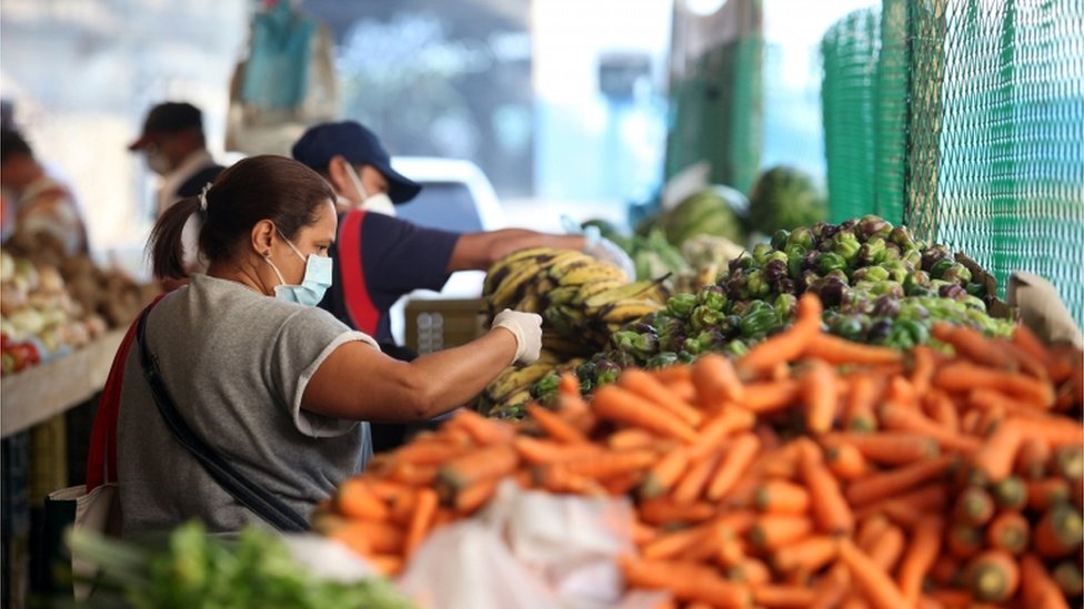 Женщина в защитной маске собирает овощи на уличном рынке во время общенационального карантина в ответ на распространение коронавирусной болезни (COVID-19) в Каракасе, Венесуэла, 31 марта 2020 года.