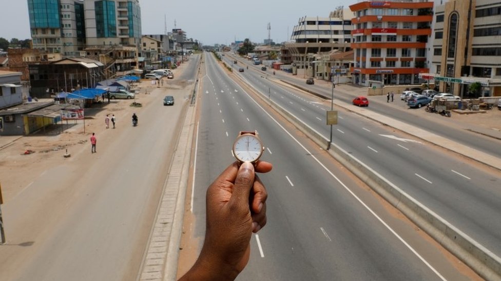 Часы, показывающие время в полдень, отображаются на фотографии, когда люди проходят мимо Центральной улицы кольцевой дороги, которая почти пуста во время вспышки коронавируса (COVID-19) в Аккре, Гана, 31 марта 2020 г.