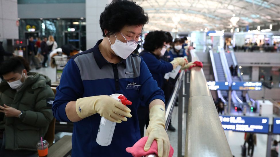 Mujer desinfectando pasamanos en un aeropuerto surcoreano.