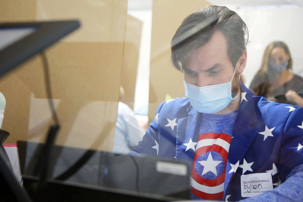 A poll worker is seen behind protective plexiglass