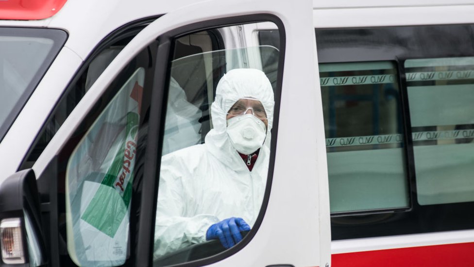 A hospital worker wearing protective equipment stands next to an ambulance in Padova, Italy