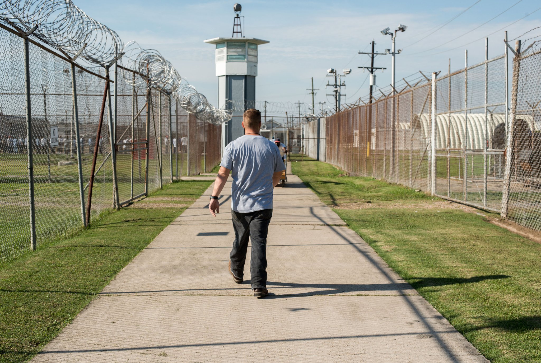 Заключенный идет через огороженный участок к сторожевой вышке в тюрьме штата Луизиана, также известной как Ангола