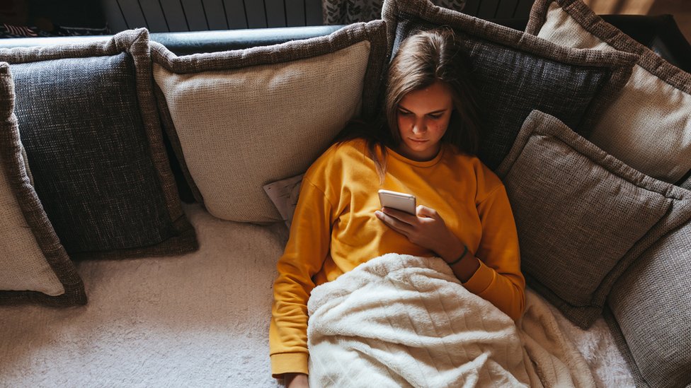 Una chica mira su teléfono inteligente sentada en un sofá