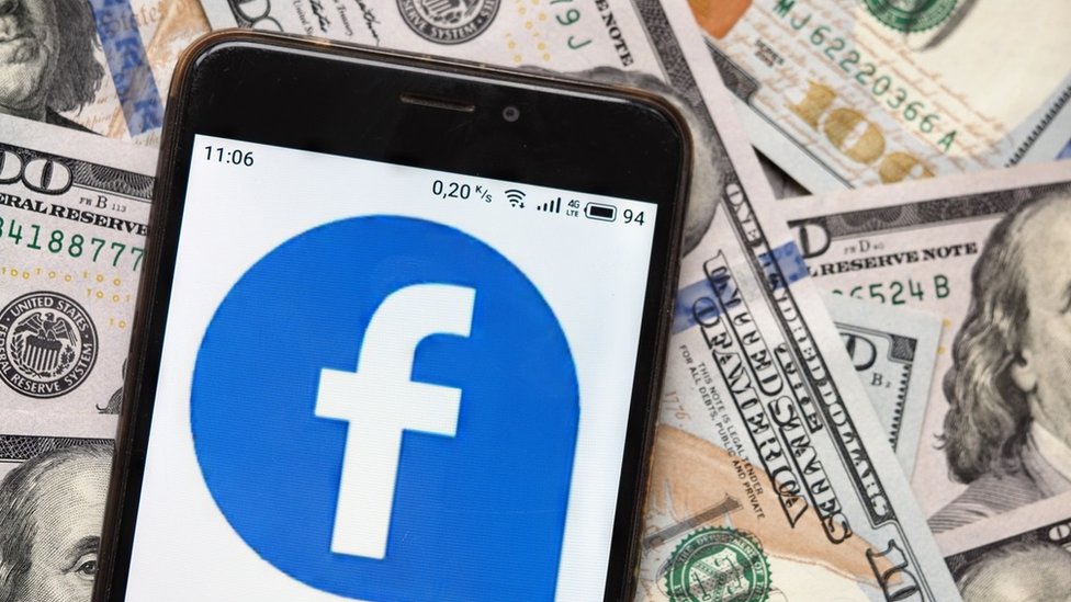 Логотип Facebook на телефоне на фоне долларовых купюр