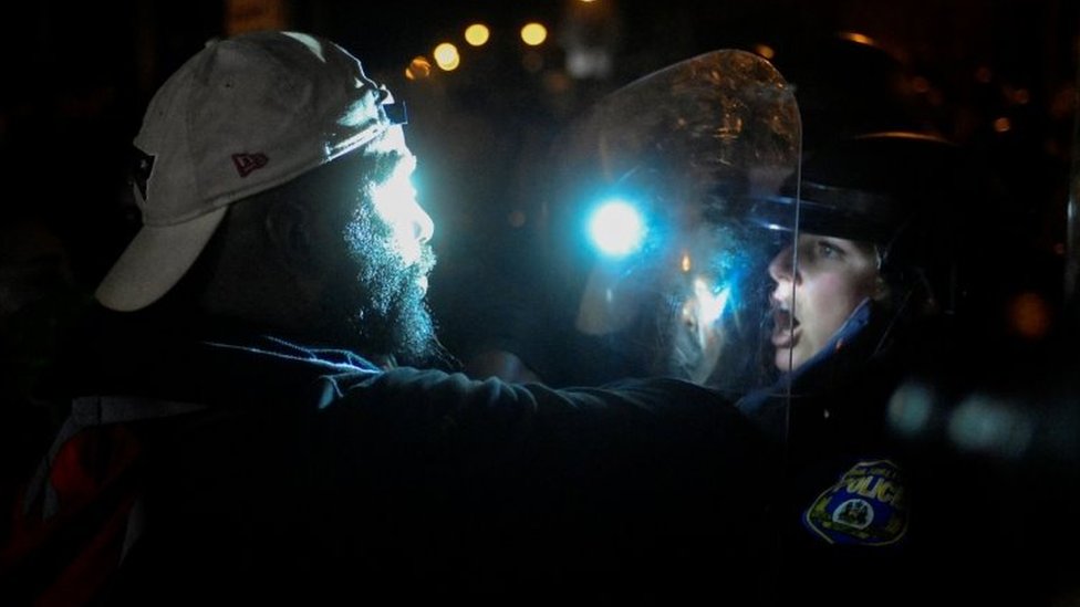 A protester faces an officer in riot gear