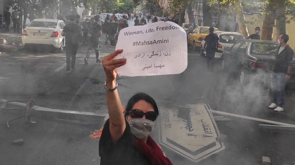 Uma mulher iraniana com a cabeça descoberta mostra uma placa com o slogan 