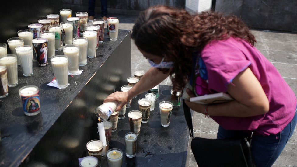 A woman places a candle at a memorial dedicated to COVID-19 victims at Basilica of Guadalupe, in Mexico City