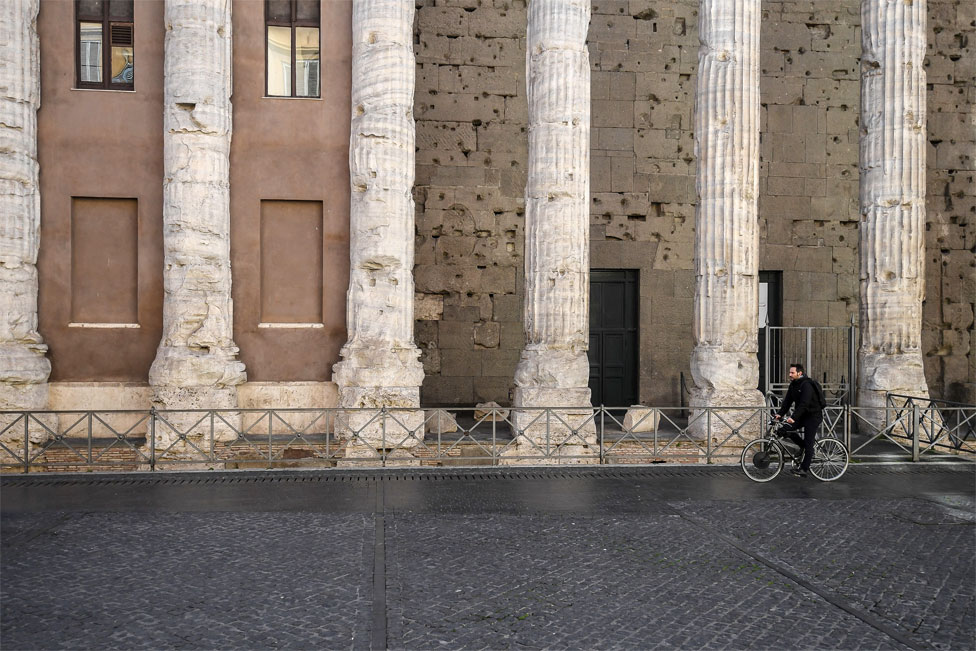 A man rides a bike past ancient stone columns