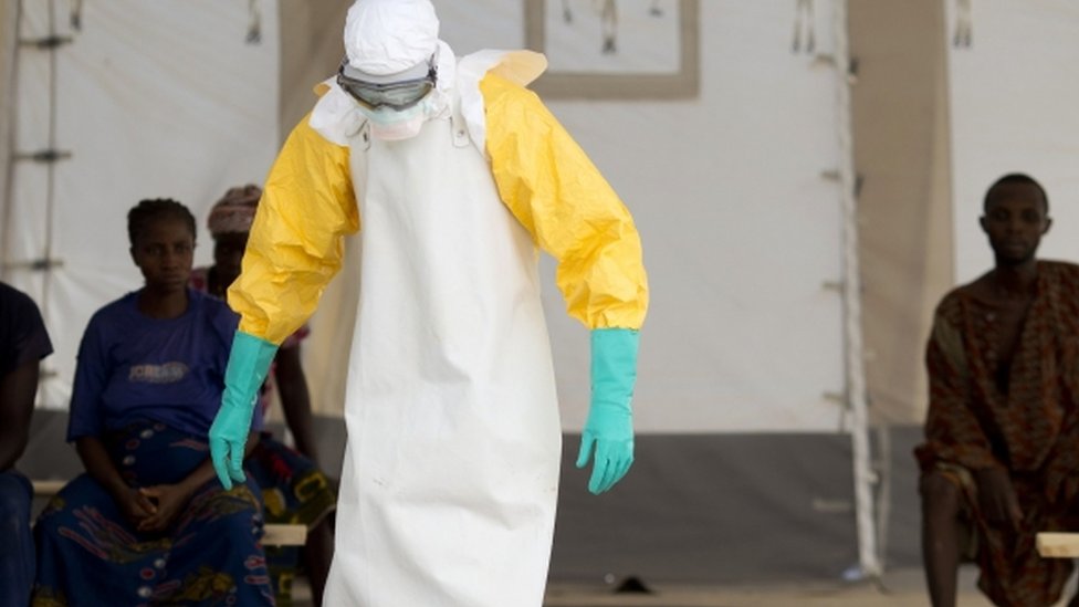 Медицинский работник в защитном костюме лечит пациентов с Эболой в Западной Африке
