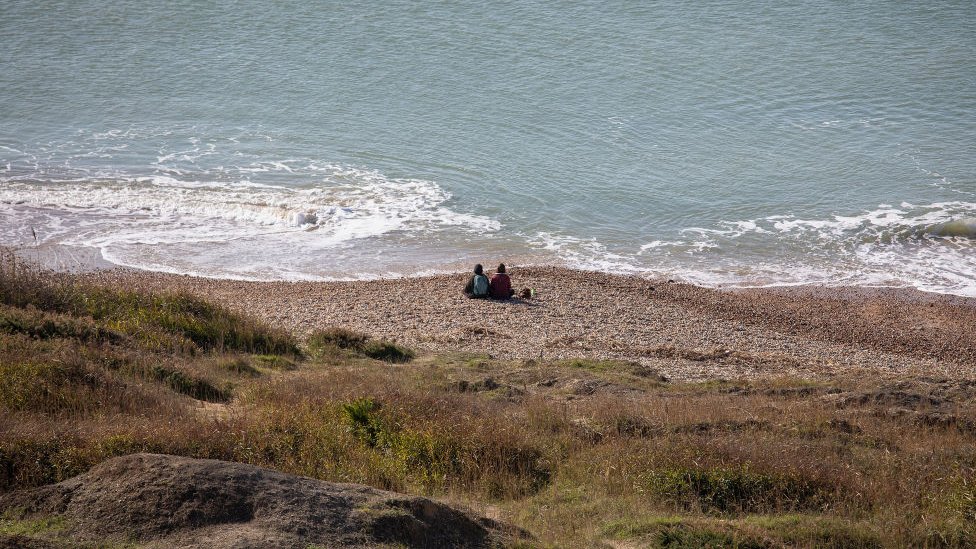 Dos personas sentadas en la costa sur de Inglaterra.