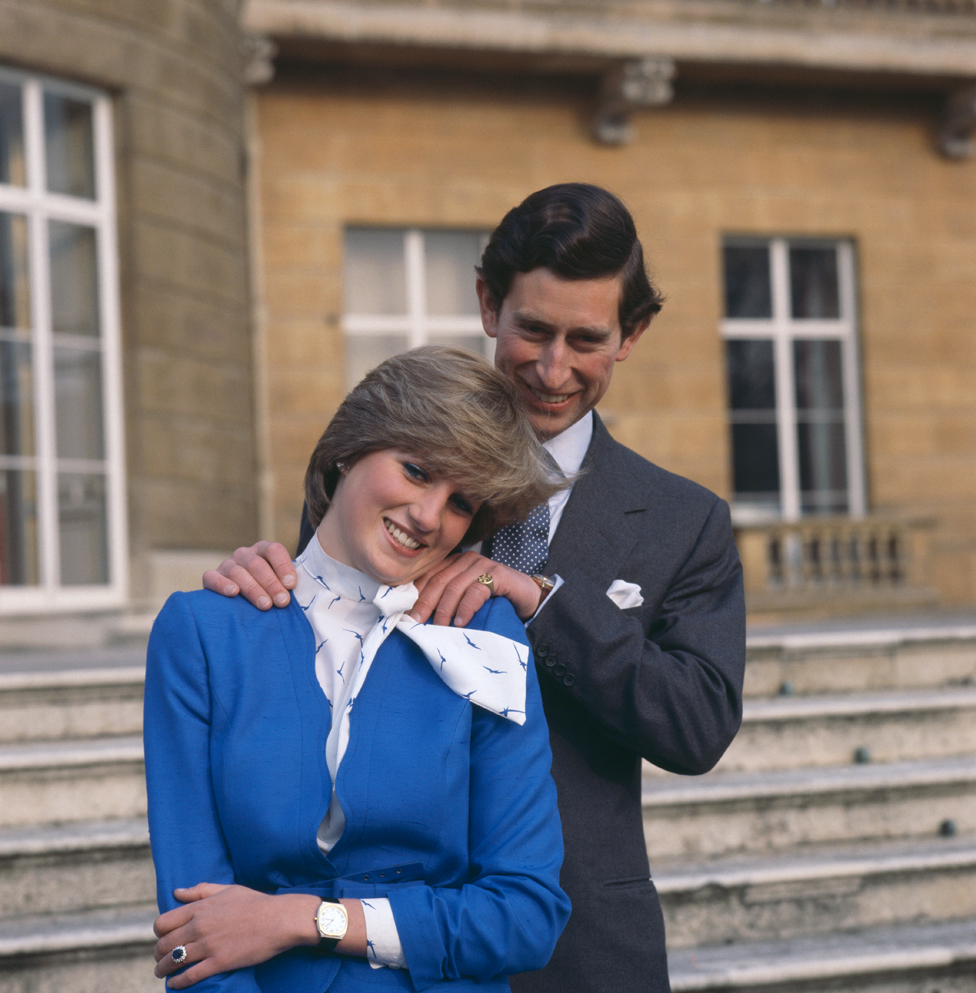 El rey Carlos III sonriendo junto a su prometida, Lady Diana Spencer, frente al Palacio de Buckingham, después de anunciar su compromiso, el 24 de febrero de 1981.