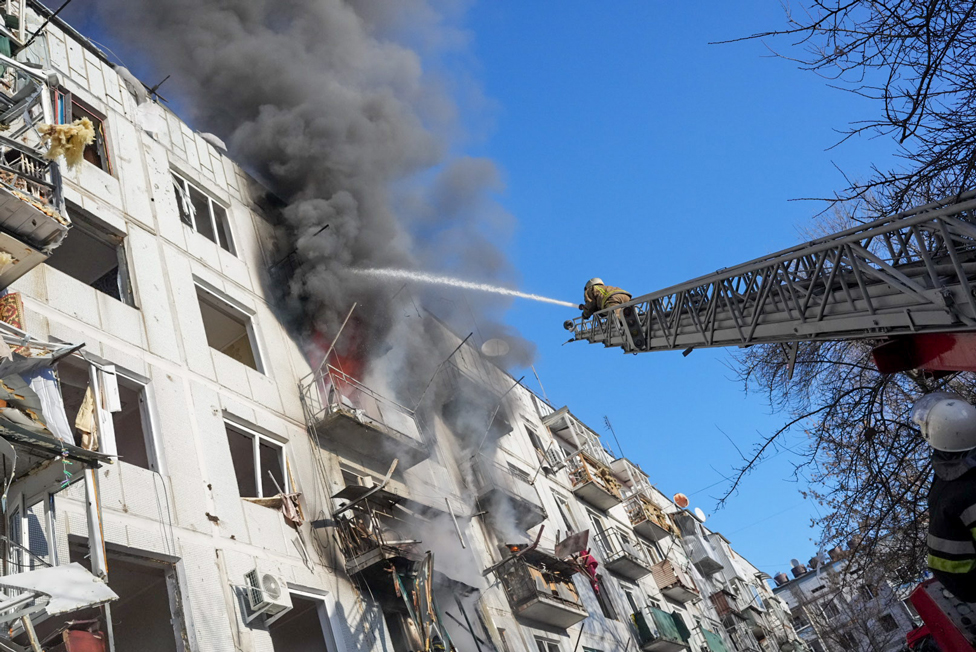 Bomberos ucranianos intentan extinguir el fuego de un complejo de apartamentos en Chugúyev, en el óblast de Járkov, que fue alcanzado por un ataque aéreo. (24 de febrero)
