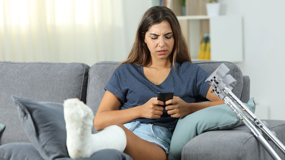 Una mujer con la pierna rota mirando su celular