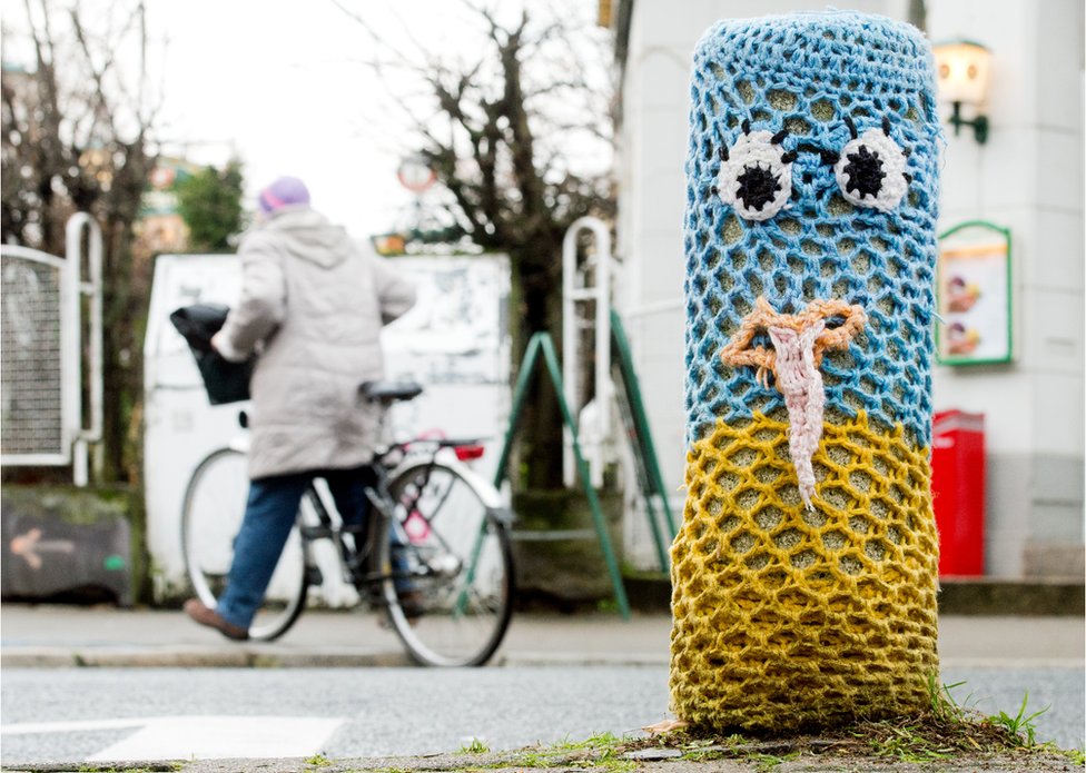 Бетонный столбик в Ганновере, Германия, покрыт яркой трикотажной тканью с двумя глазами и ртом - пример бомбардировки пряжей