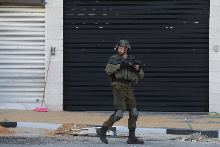جندي إسرائيلي يمر من أمام المحلات المغلقة في الموقع حيث قتلت قواته ثلاثة فلسطينيين بالرصاص، بالقرب من حاجز صرة العسكري خارج مدينة نابلس بالضفة الغربية، 12 مارس/آذار 2023.