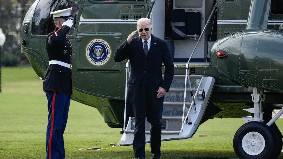Joe Biden walking out of a helicopter in a large coat and sunglasses 