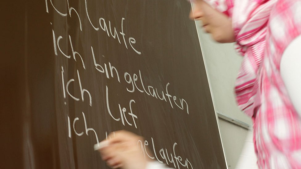 Девушка в платке пишет на доске по-немецки