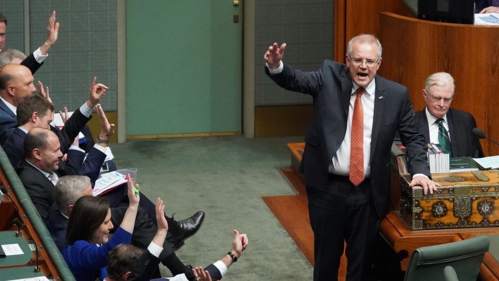 Премьер-министр Австралии Скотт Моррисон и несколько депутатов правительства поднимают руки в Палате представителей