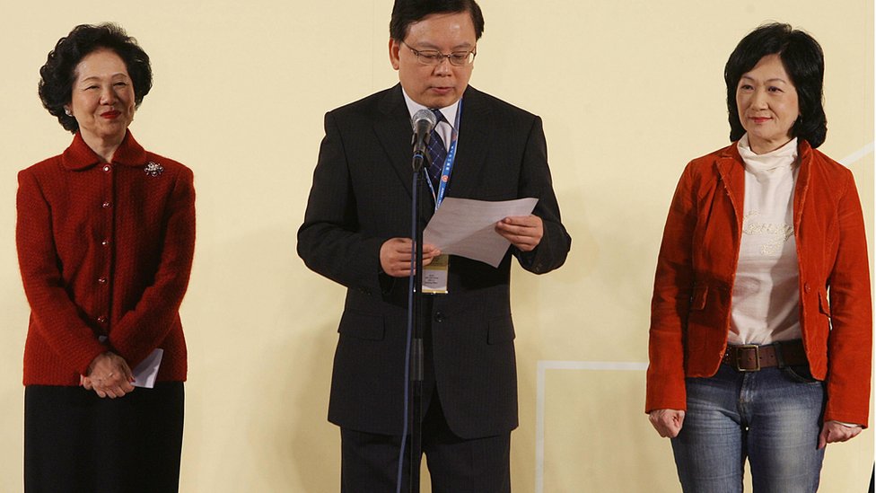 Ведущий про-демократ Ансон Чан (слева) и соперница на выборах Регина Ип (справа) слушают вернувшегося офицера в Гонконге 03 декабря 2007 г.