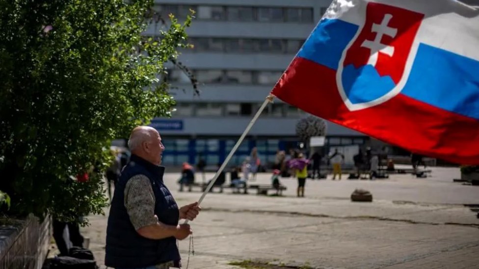 Čovek maše slovačkom zastavom ispred bolnice u kojoj Fico ostaje u ozbiljnom stanju