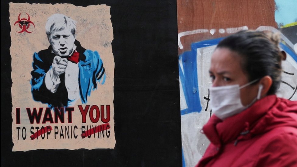 Una mujer con tapaboca pasa delante de un cartel de arte callejero en Londres con Boris Johnson diciendo: "Quiero que entres en pánico".