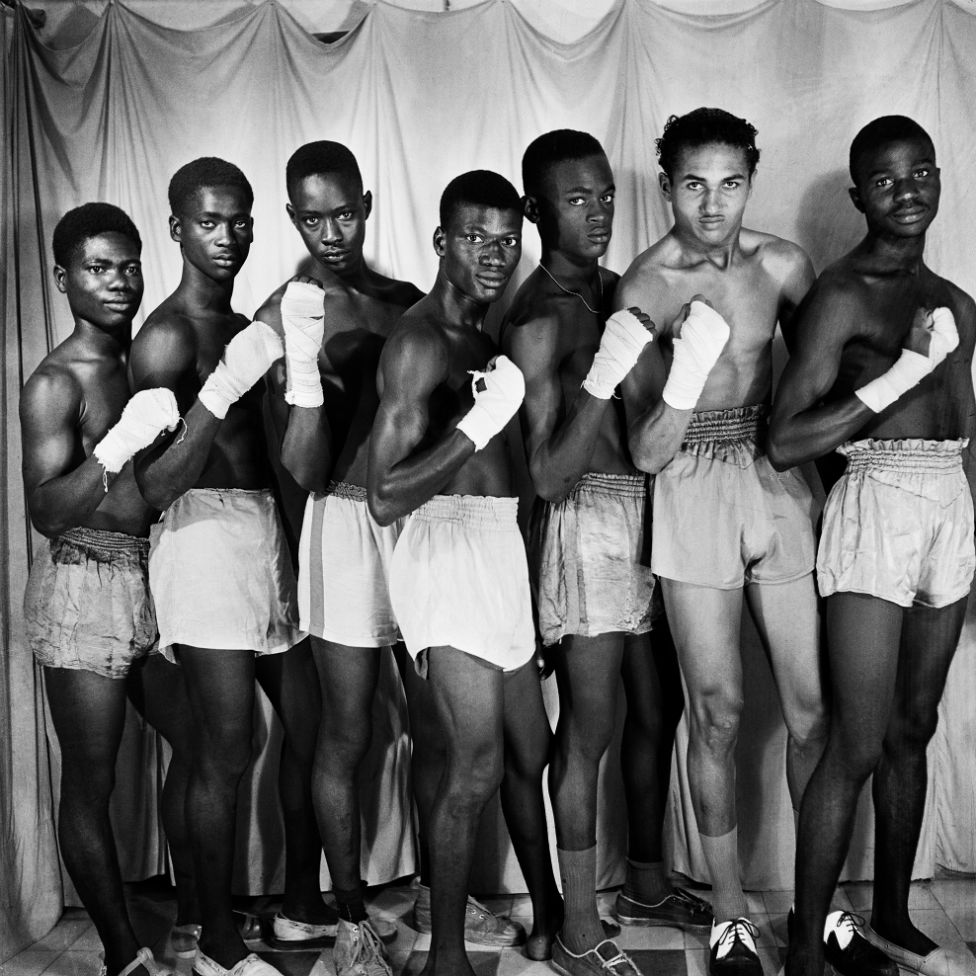 Men dressed in boxing shorts with bandaged hands pose in a line for the camera.