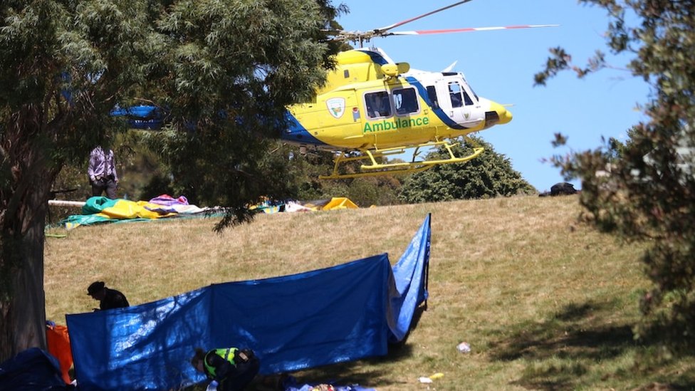 An ambulance helicopter seen next to a deflated bouncy castle and a tarpaulin on a hill