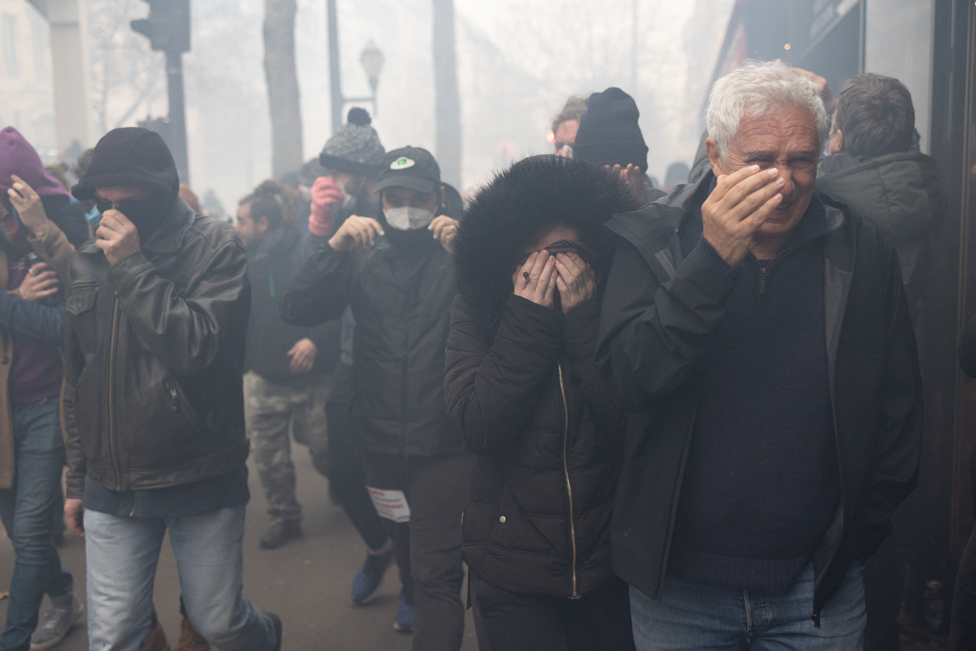Protesters shield their eyes from tear gas during a demonstration, a week after the government pushed a pensions reform through parliament without a vote, using the article 49.3 of the constitution, in Paris on March 23, 2023.