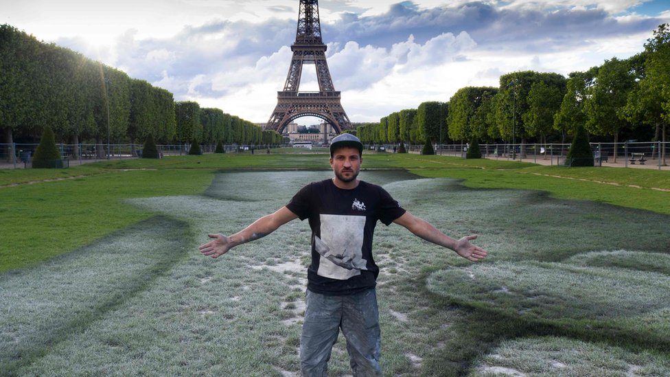 French street artist Saype poses at the Eiffel Tower in front of his giant artwork "Beyond Walls"