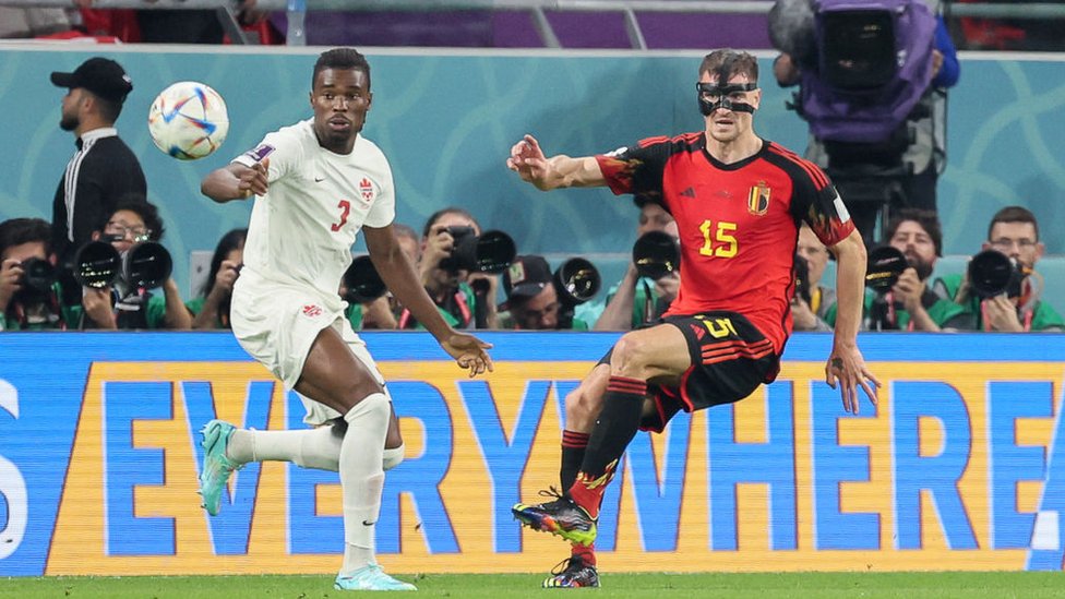 El defensa belga Thomas Meunier (derecha) con una máscara negra que cubre parte de su cara y el defensa canadiense Sam Adekugbe en el partido debut de ambas selecciones en Qatar 2022 el 23 de noviembre.