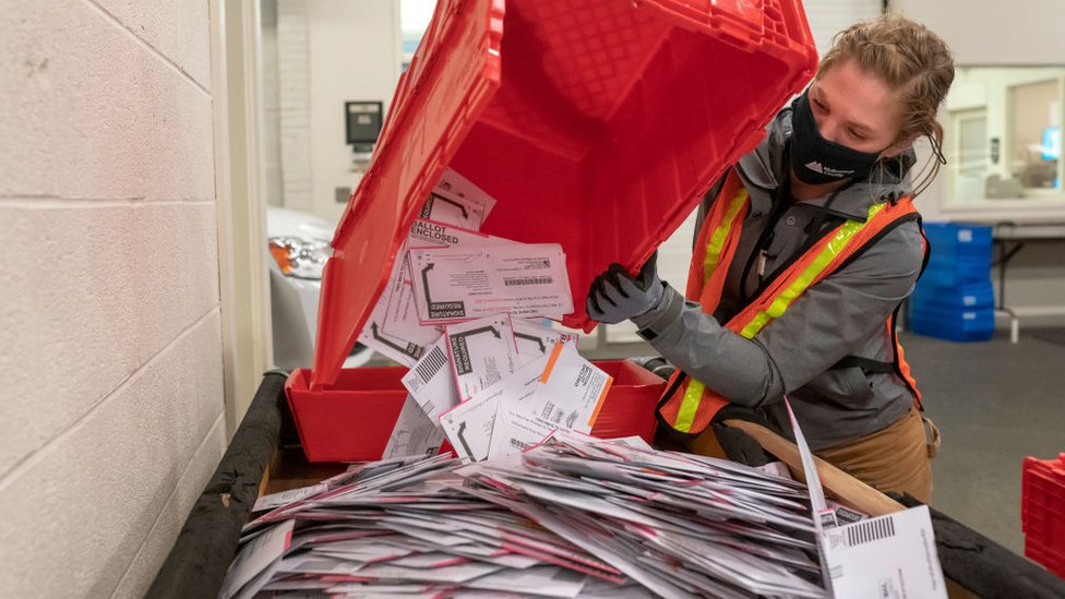 Una trabajadora postal con una cesta llena de votos por correo.