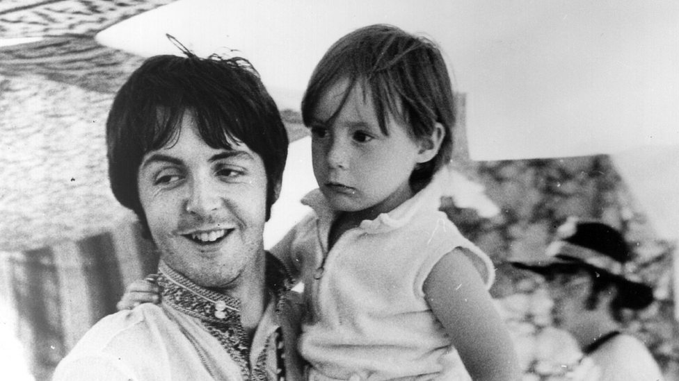 Пол Маккартни держит четырехлетнего Джулиана, сына своего коллеги Джона Леннона (на заднем плане) во время отпуска