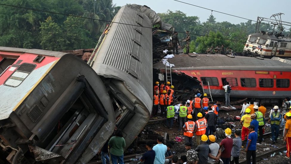 Rescue workers gather around damaged carriages at the accident site of a three-train collision near Balasore