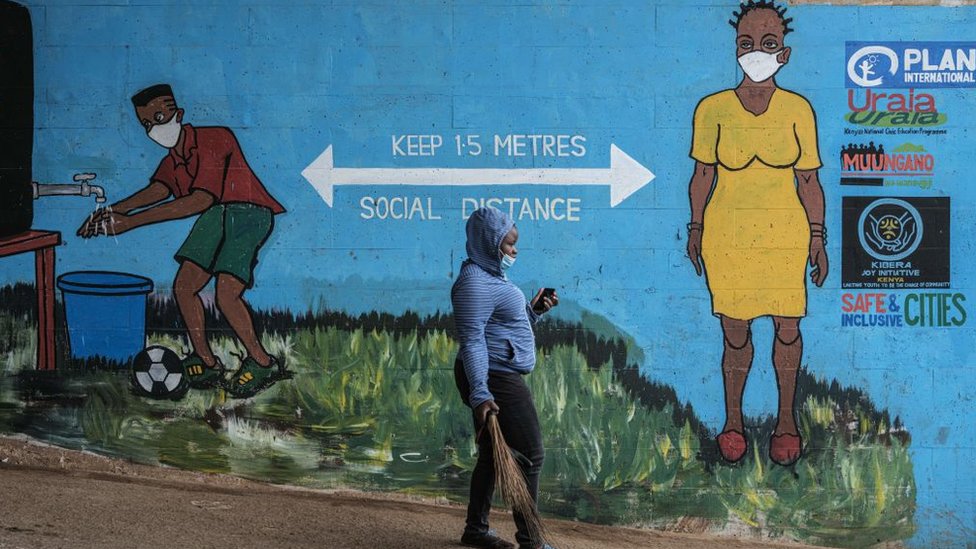 Женщина в маске проходит мимо граффити, которое поощряет социальное дистанцирование, чтобы обуздать распространение коронавируса COVID-19, в Кибере, Найроби, 15 июля 2020 года.