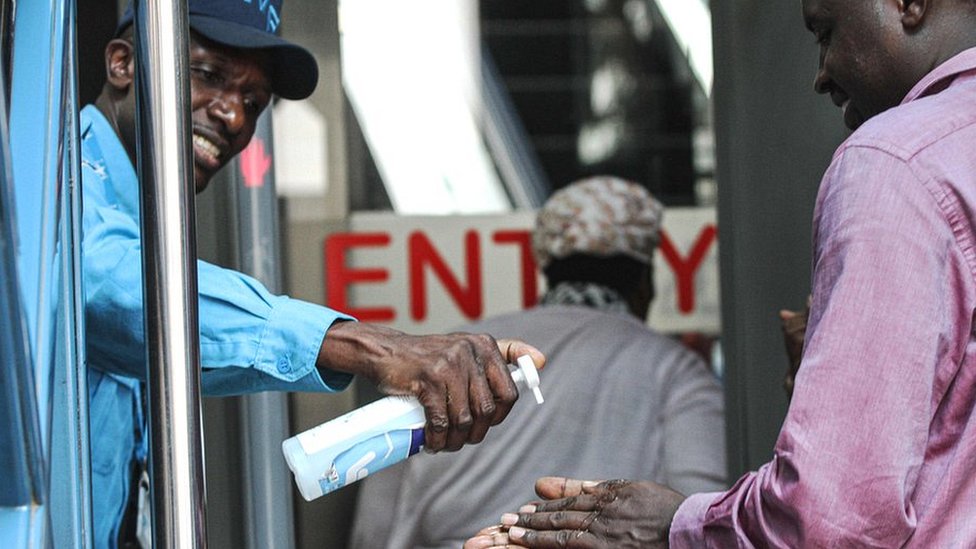 Охранник дает посетителям дезинфицирующее средство для рук в качестве меры предосторожности у входа в здание в Найроби, Кения - 13 марта 2020 г.