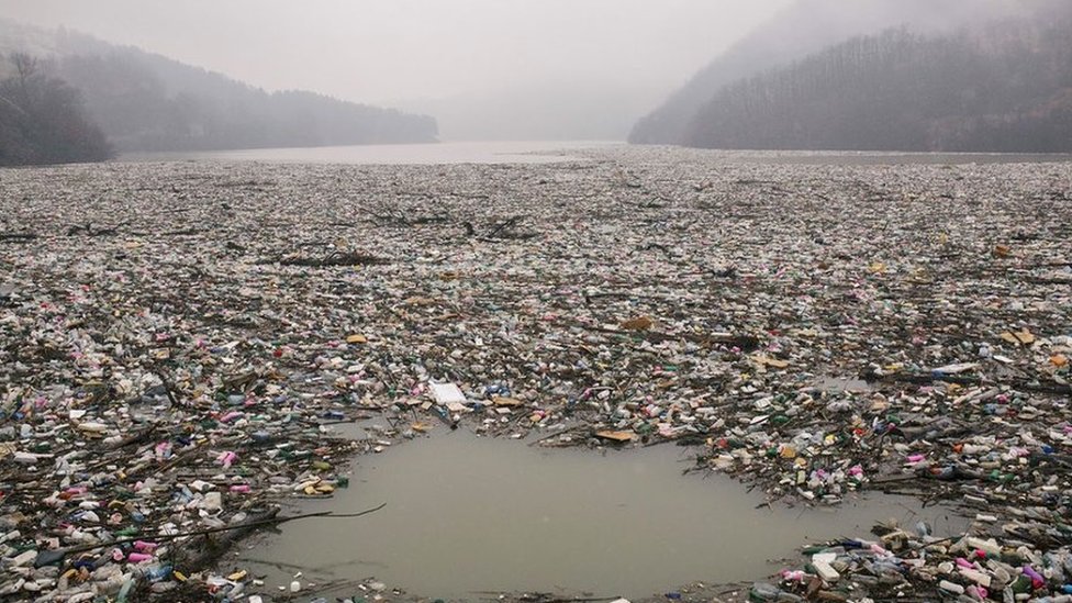 A lake at the bottom of mountains filled with rubbish floating on the surface
