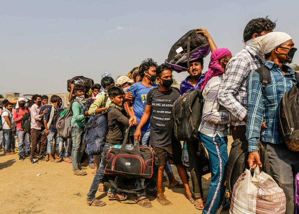 Трудящиеся-мигранты со своими семьями выстраиваются в очередь в ожидании посадки в автобусы домой.