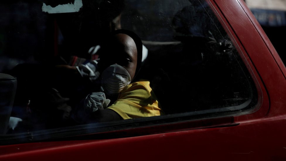 Мальчик в защитных перчатках и маске едет в фургоне после того, как правительство Гаити объявило чрезвычайное положение