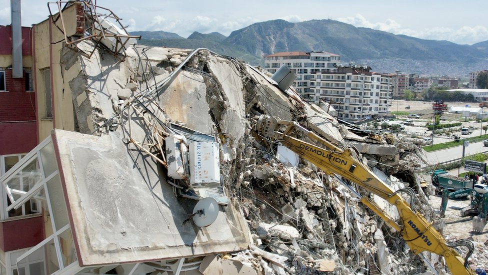 A digger working on the wreckage of a collapsed building in Antakya