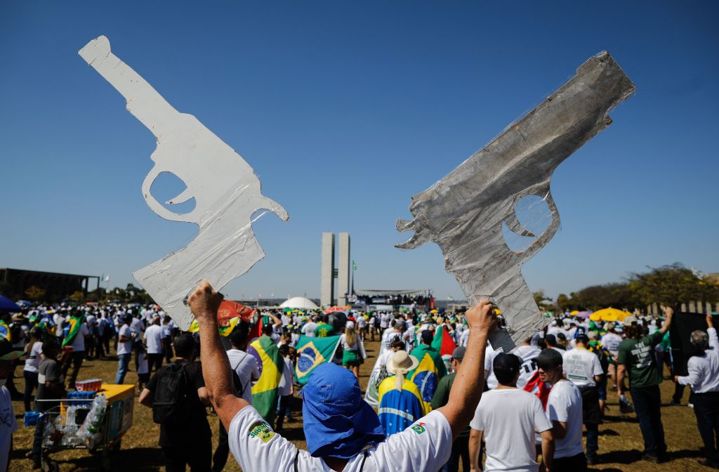 Un hombre muestra dos carteles con forma de revólver durante una manifestación pro/armas en apoyo a Bolsonaro en Brasilia.