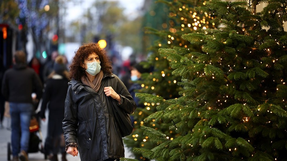 Woman in mask next to Christmas tree