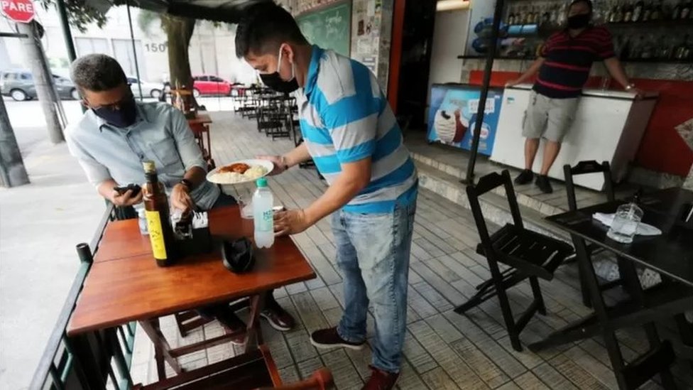 Garçom serve refeição a cliente em restaurante aberto